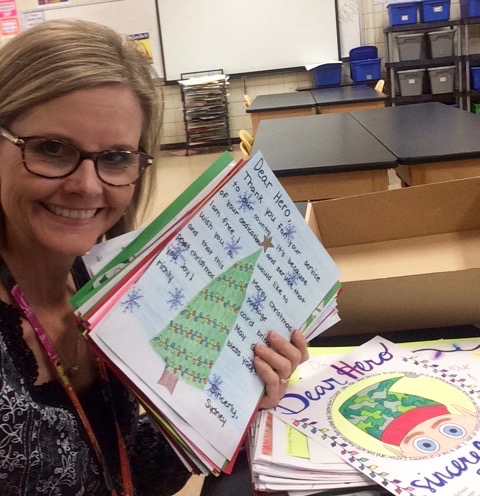 Art teacher poses with the holiday cards her students made for deployed military 